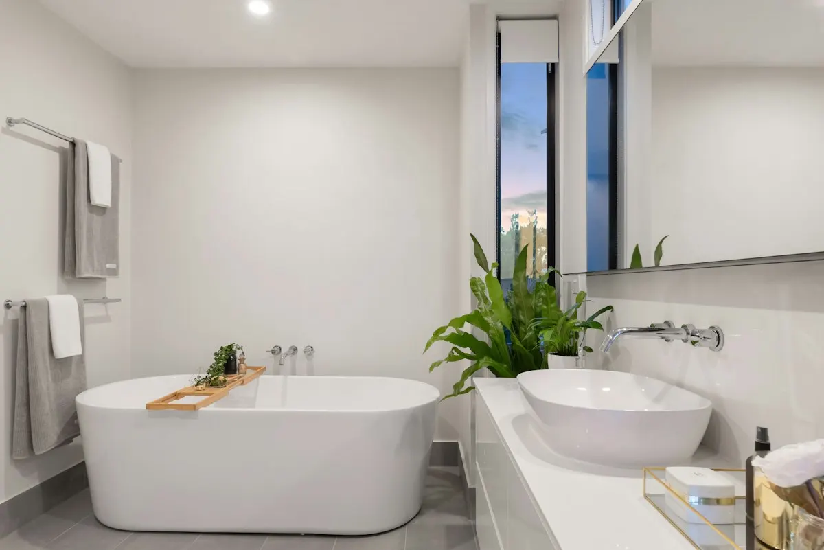 White freestanding bath beside a window and double basin